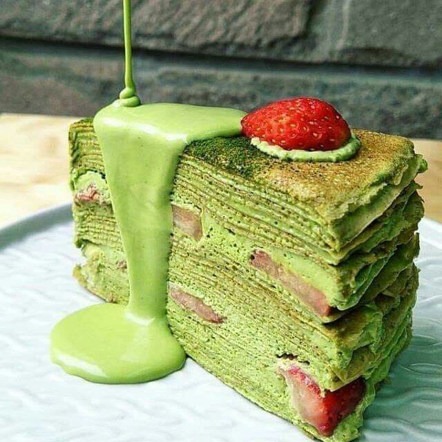 Slice of matcha crepe cake with green glaze and a strawberry on top