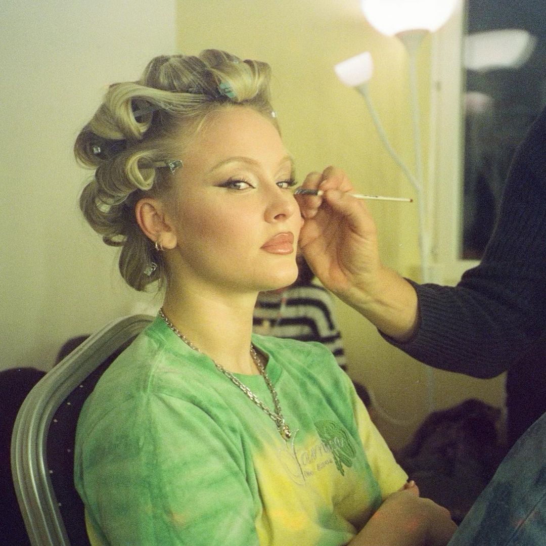 Young woman with hair in curlers getting makeup applied backstage in a dressing room