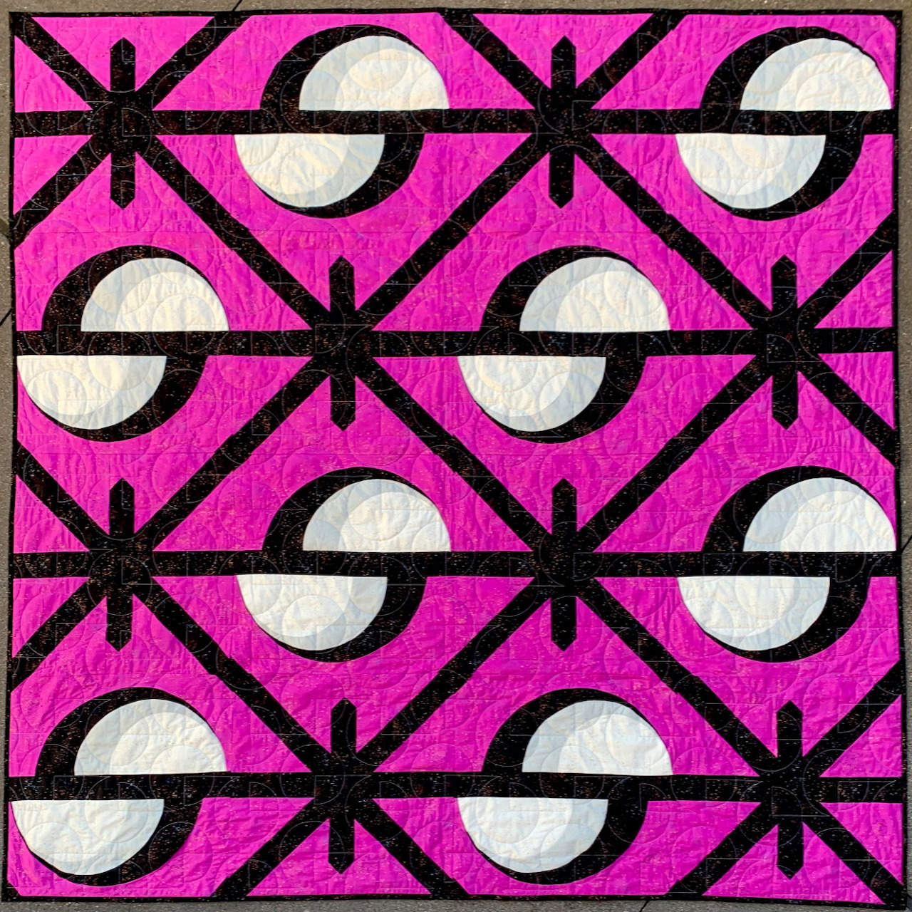 Geometric quilt with black stars, white circles on bright pink background in repeating diamond pattern
