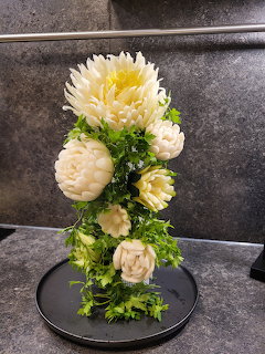 White and cream floral arrangement with green leaves on a round black tray indoors