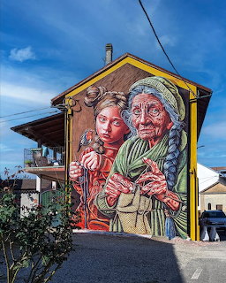 Large colorful mural of two people painted on yellow building facade under blue sky