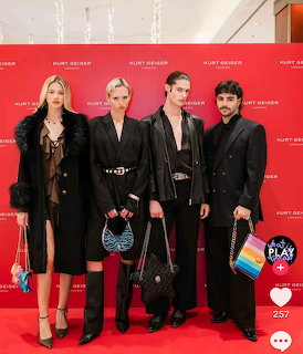 Four models in black outfits posing on a red carpet in front of a red branded backdrop