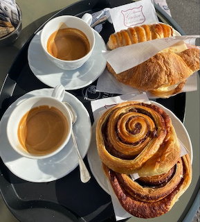 Two cups of coffee with croissants and spiral pastries on a black tray