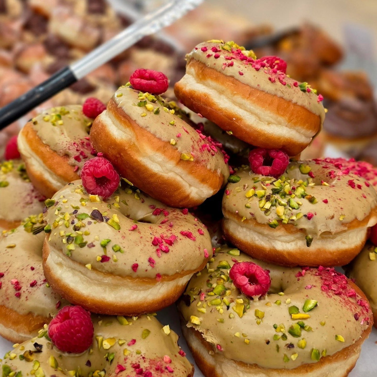 Glazed doughnuts topped with crushed pistachios and fresh raspberries stacked together
