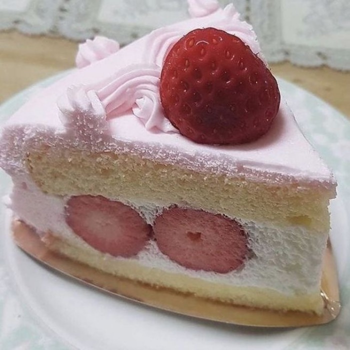Slice of pink strawberry shortcake with fresh berries and whipped cream on white plate