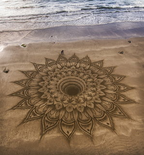 Elaborate mandala pattern etched in wet sand on beach with ocean waves