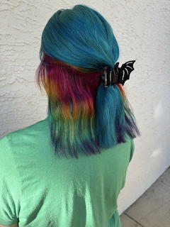 Back view of a woman with blue and rainbow dyed hair and a black bat hair clip