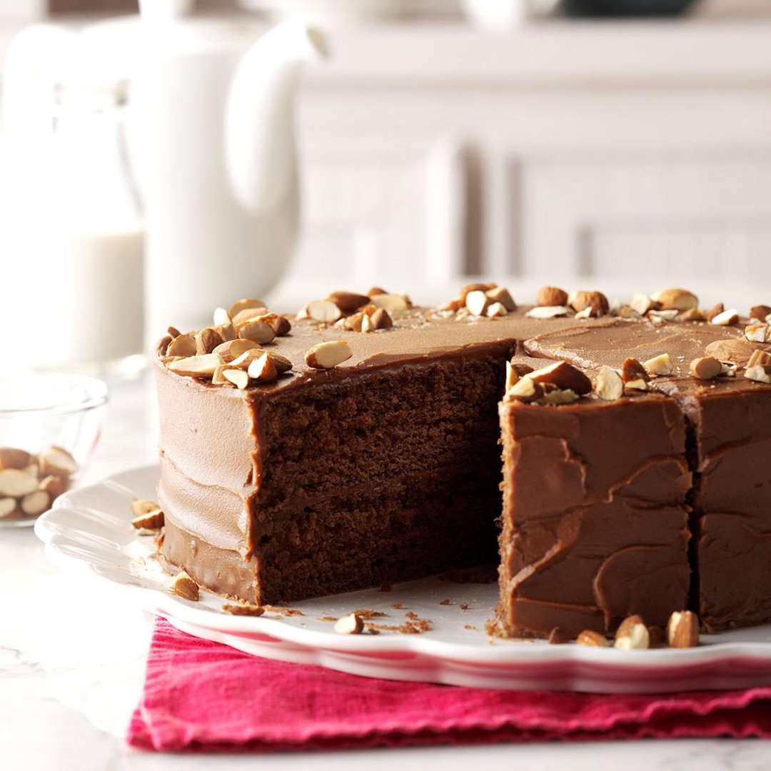 Chocolate layer cake with frosting and nuts on white stand, one slice cut