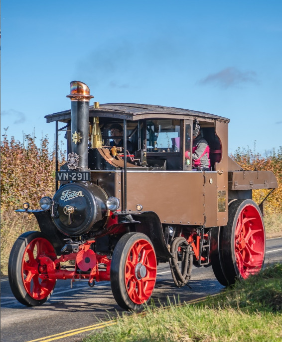 Vintage steam tractor with red wheels on a country road beside a field