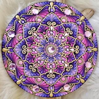 Circular purple mandala with detailed dot painting patterns in pink, gold, and white on geometric symmetrical design