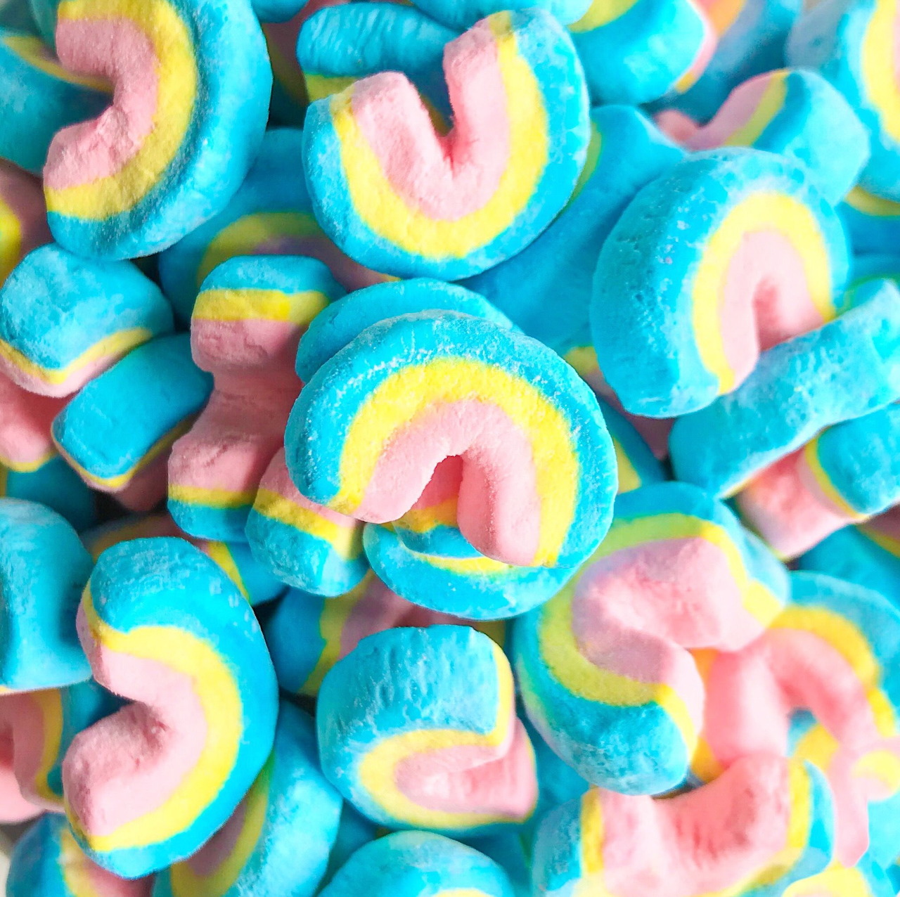 Pile of rainbow-striped Lucky Charms marshmallows in blue, pink, yellow and white colors