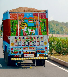 Rear view of colorfully decorated Indian truck with painted tropical scenes and ornate details on road