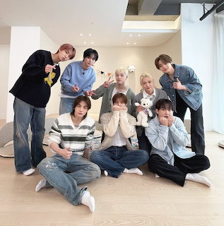 Seven young men from Stray Kids posing together indoors in a bright modern room