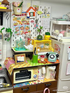 Colorful miniature dollhouse kitchen with tiny furniture, appliances, and decorative accessories on multiple shelves