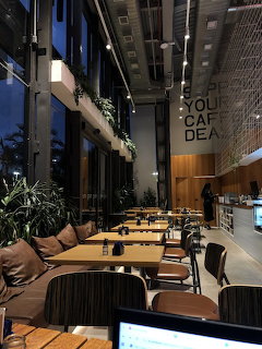 Modern cafe interior with wooden tables, black chairs, plants, and industrial design elements