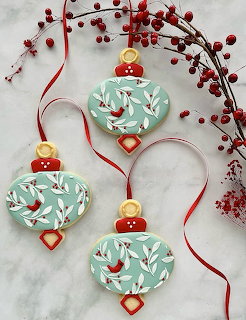 Three turquoise heart ornaments with red birds hanging by red ribbons alongside red berry branches