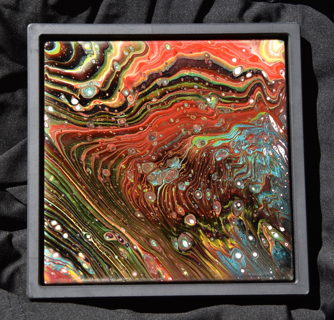 Framed abstract pour painting with swirling red, gold, black, and blue patterns