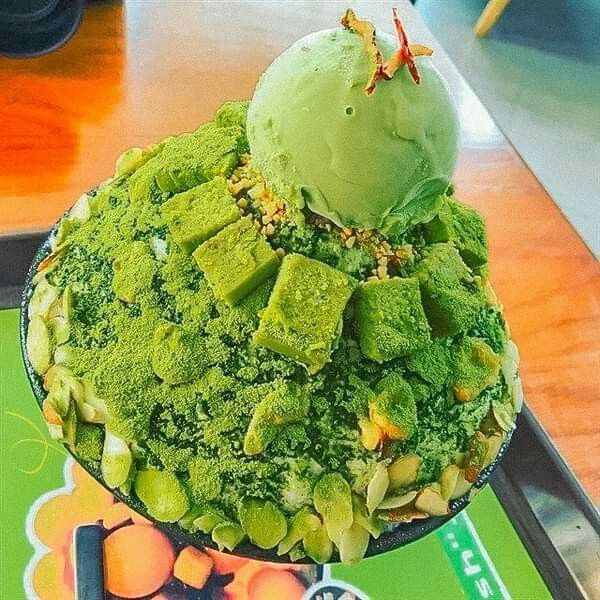 Bowl of green matcha shaved ice topped with ice cream scoop and matcha powder