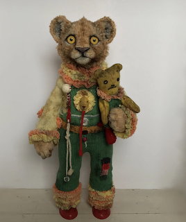 Vintage handmade teddy bear in green overalls and patchwork jacket holding a smaller teddy bear