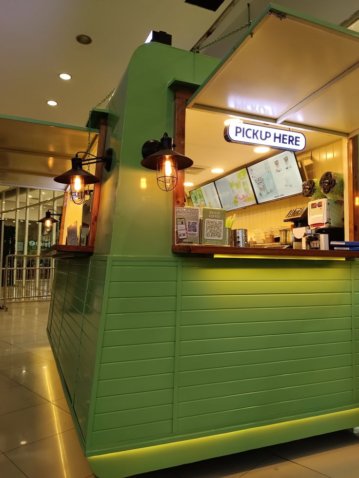 Green coffee shop kiosk with pickup counter, pendant lights, and menu boards inside a mall