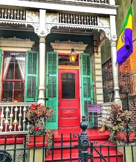 Ornate Victorian house entrance with bright red door, turquoise shutters, white decorative trim, and colorful porch