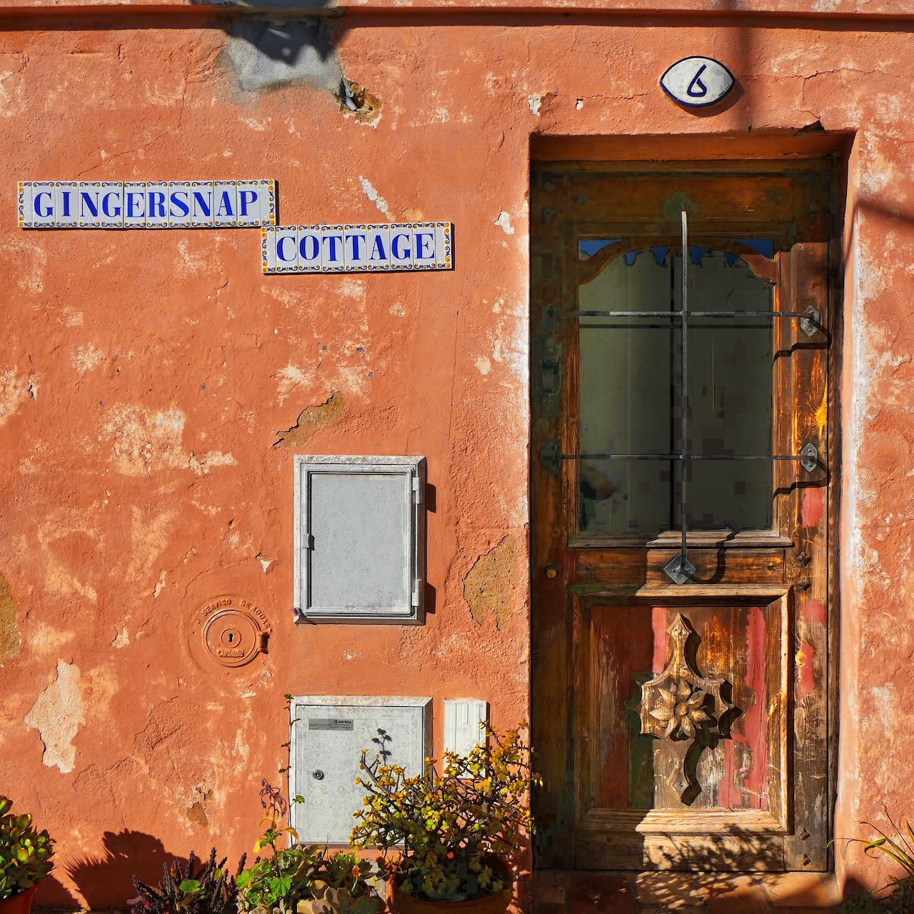 Weathered orange cottage wall in Portugal with old green door and vintage street signs