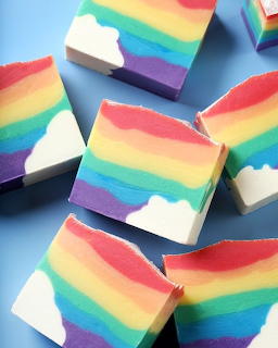 Multiple rainbow-striped handmade soap bars with white bases displayed on blue surface