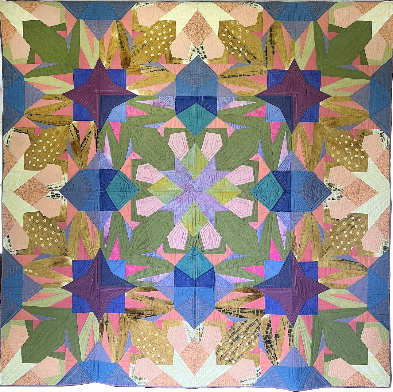 Symmetrical textile quilt with geometric patchwork in blue, green, pink, and gold forming kaleidoscopic pattern