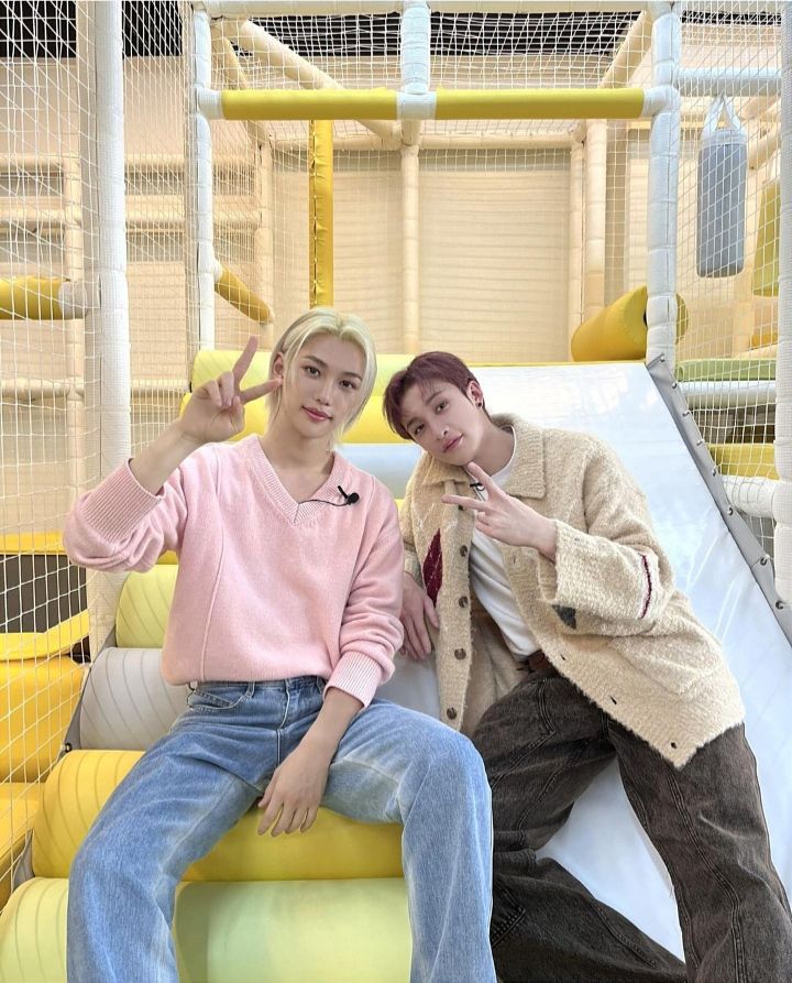 Two young men smiling and making peace signs at a yellow and white indoor play structure