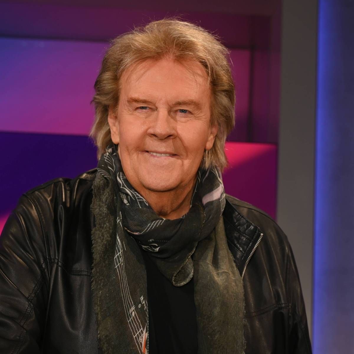 Smiling older man in a leather jacket and scarf with a purple studio background