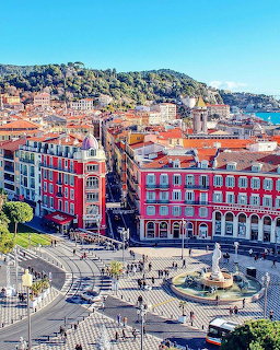 Aerial view of plaza in Nice, France with red buildings, fountain, and hillside backdrop
