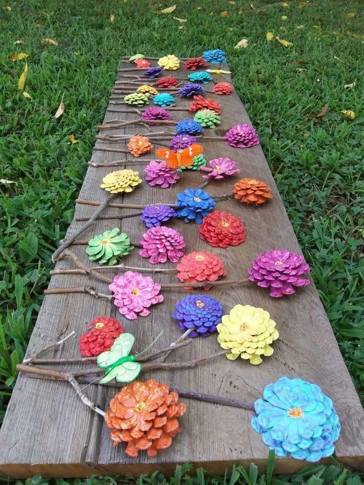 Rows of pine cones painted in bright colors to look like flowers displayed on a wooden plank on grass