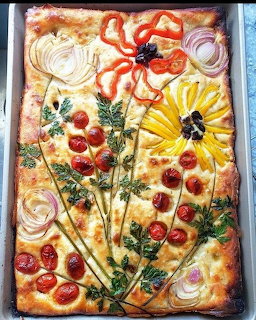 Focaccia bread decorated with vegetables arranged as flowers on a baking sheet