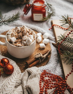 Cup of hot chocolate with marshmallows on a wooden board surrounded by Christmas decorations and a red candle