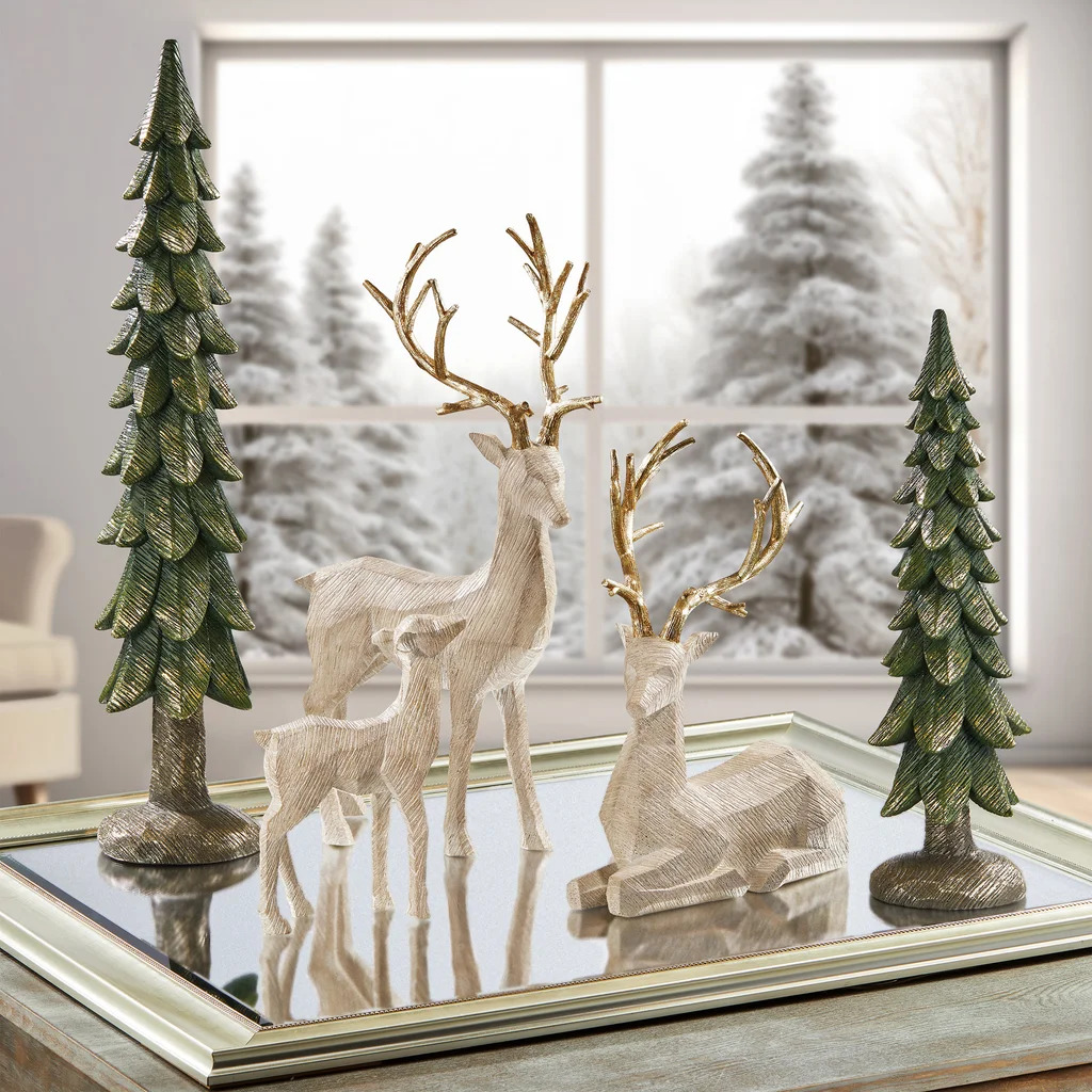 White deer figurines with gold antlers, Christmas trees, and snowy window backdrop on mirrored surface