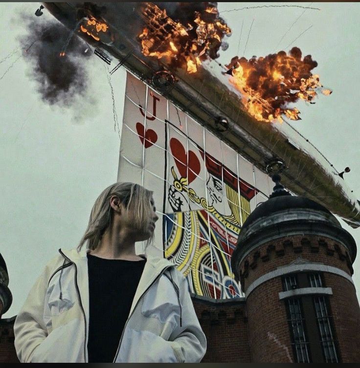 Person in white jacket looking at a building mural with rooftop explosions