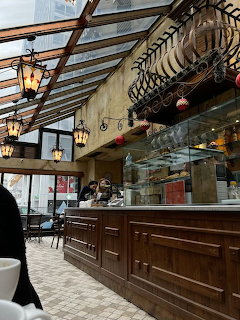Cafe interior with wooden counter, glass display case, hanging lanterns, and a glass roof