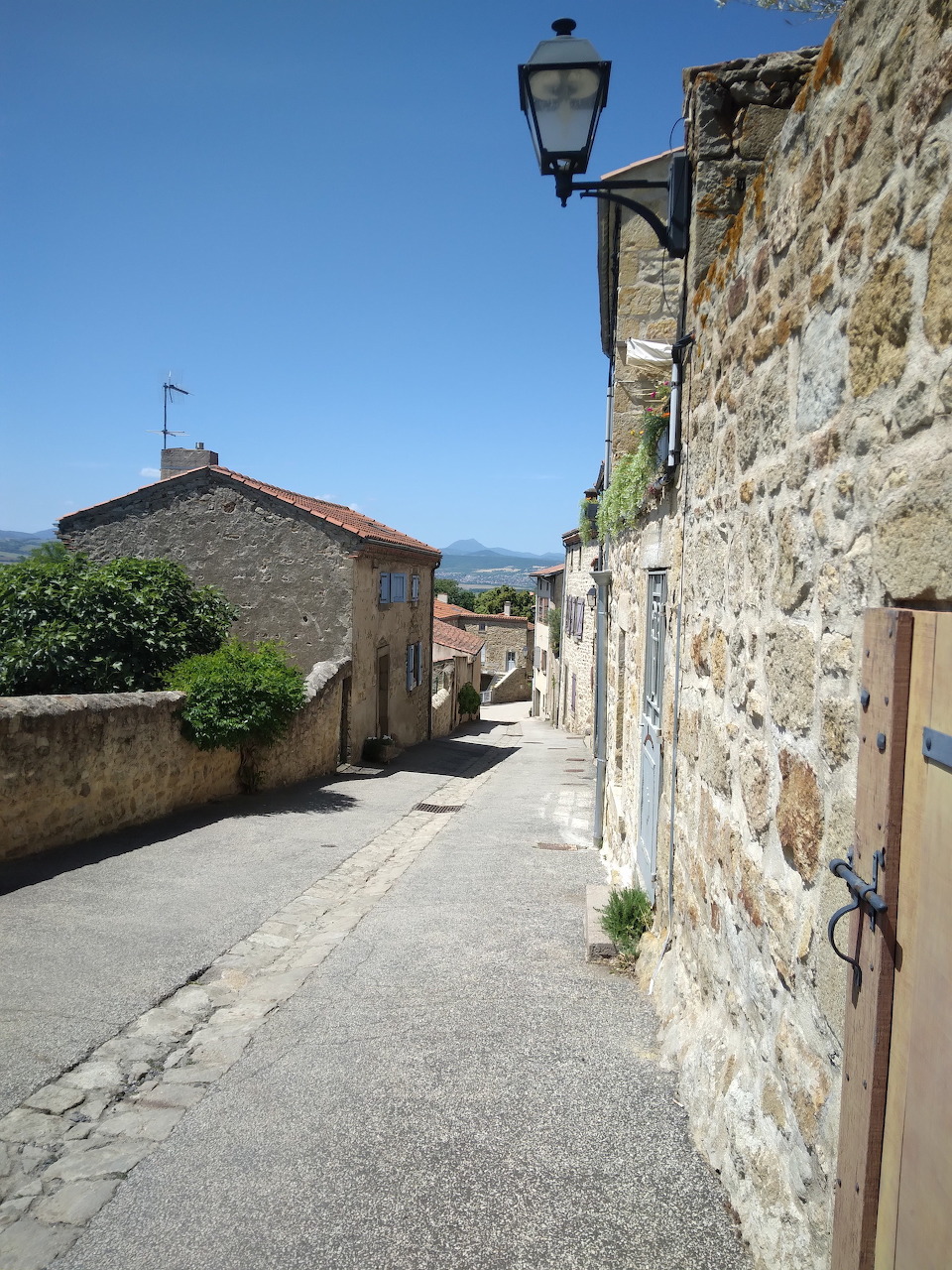 Narrow village lane beside stone houses and wall under a clear blue sky
