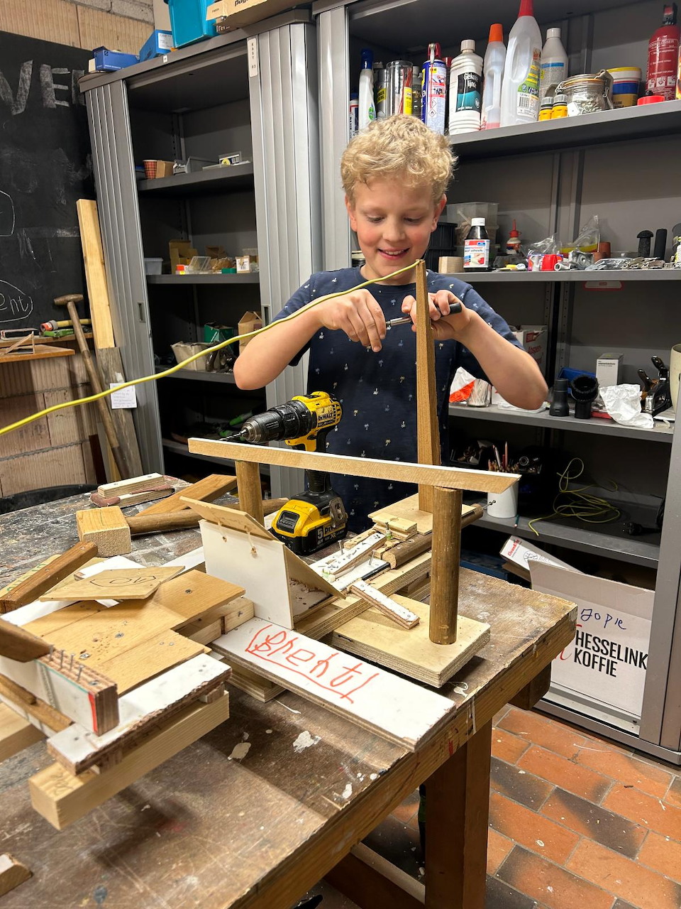Young boy assembling a wooden structure on a workbench in a workshop