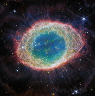 Colorful ring-shaped nebula with blue center, green and pink outer layers, and bright stars in black space