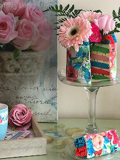 Colorful rainbow layer cake on pedestal with pink roses and gerbera daisy bouquets