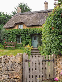 Thatched cottage with ivy walls, wooden gate and stone pathway in English countryside garden