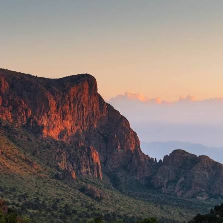 Sunset light illuminating a rugged Big Bend mountain cliff above desert vegetation.