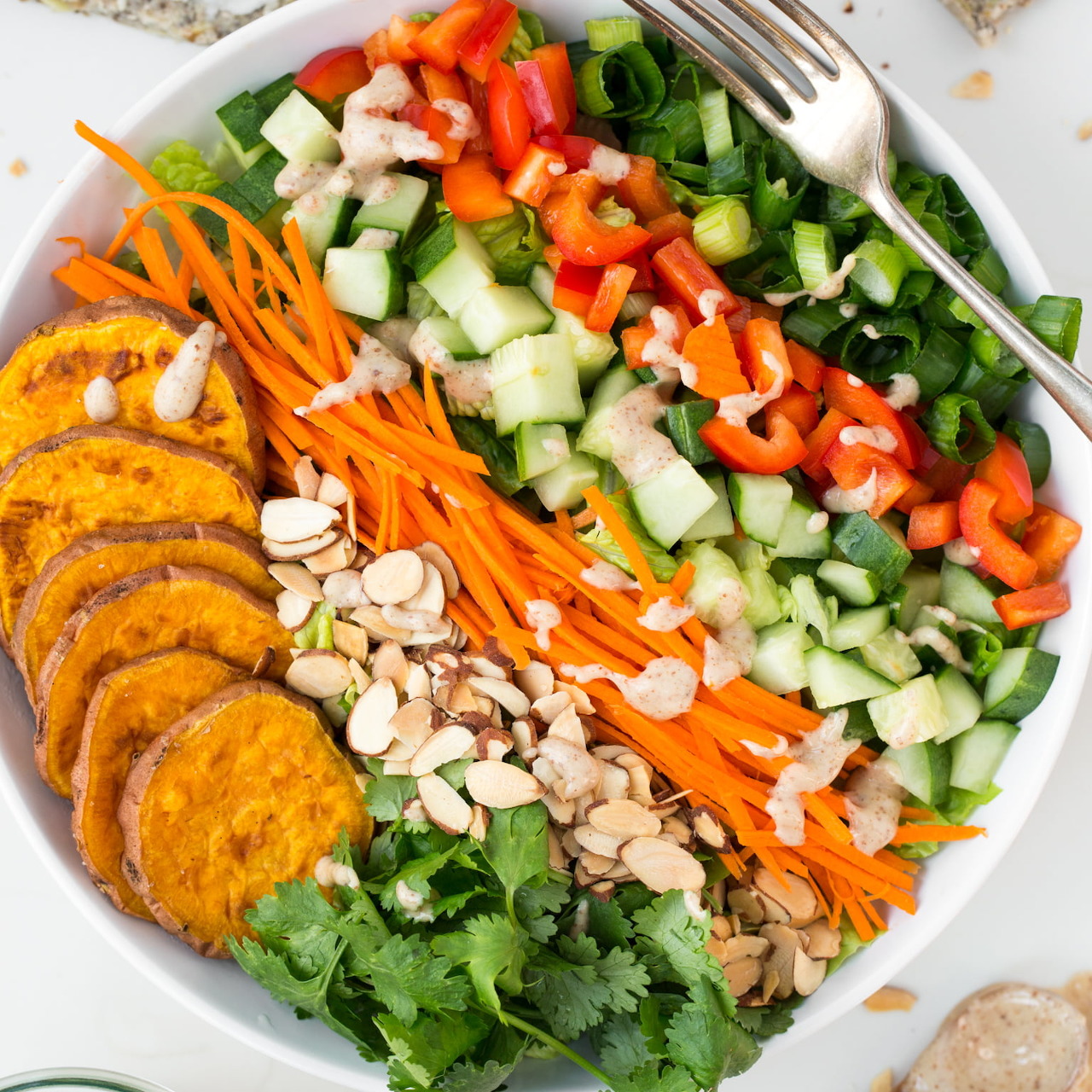 Colorful salad bowl with cucumbers, red peppers, carrots, greens, almonds, and sweet potato slices