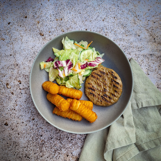 Gray plate with grilled burger, golden croquettes, and colorful fresh salad on textured surface