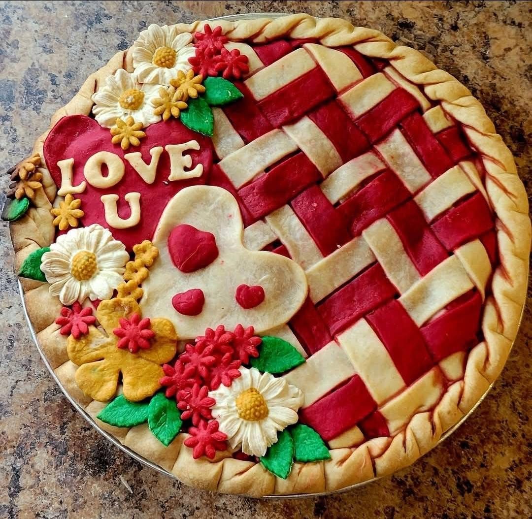Heart-decorated pie with red filling, lattice crust, flowers, and 'LOVE U' text on granite counter