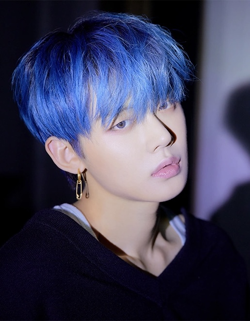 Young man with vivid blue hair and gold hoop earrings in a close-up portrait shot