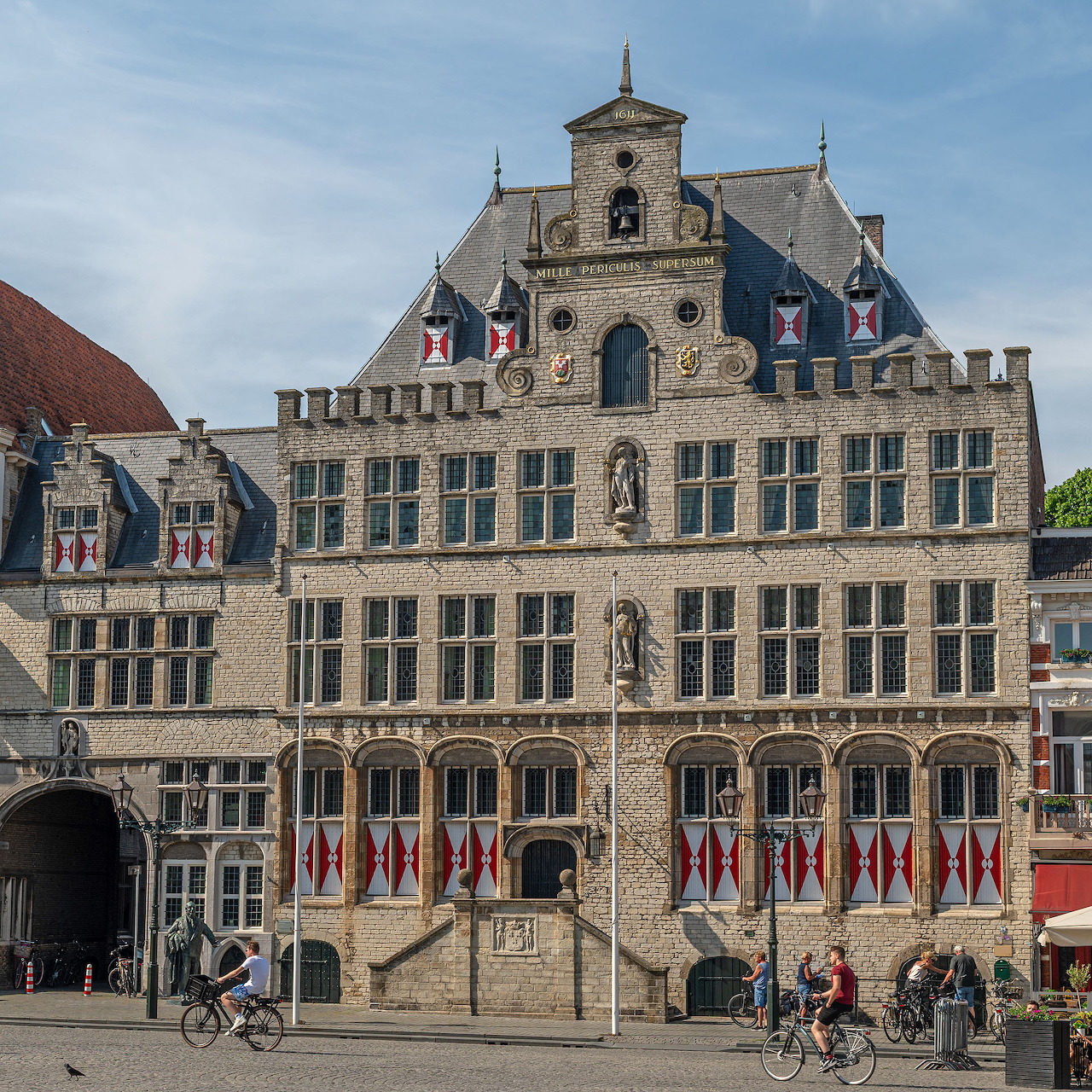 Old town hall building in Bergen op Zoom with flags, statues, and cyclists in front