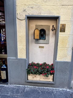 Small arched wine window in a stone wall with a flower box and wine bottle in Florence, Italy