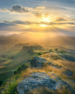 Golden sunset over rolling mountain hills with grassy ridge and layered peaks under dramatic clouds